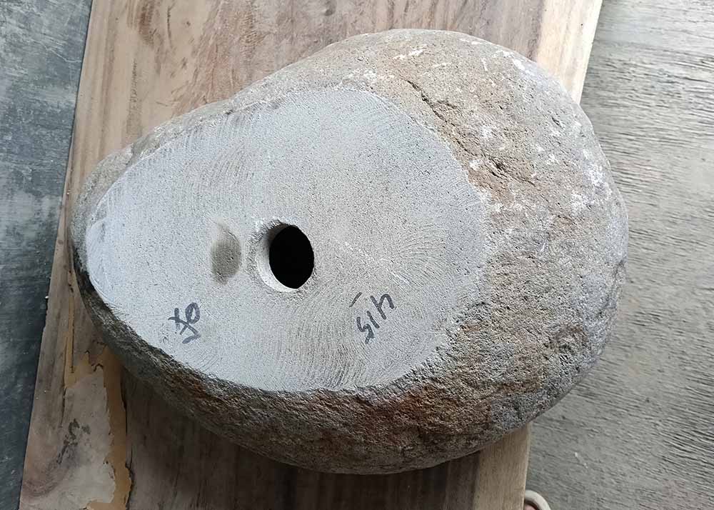 Bottom of handcrafted stone sink with drilled drain hole and flat base