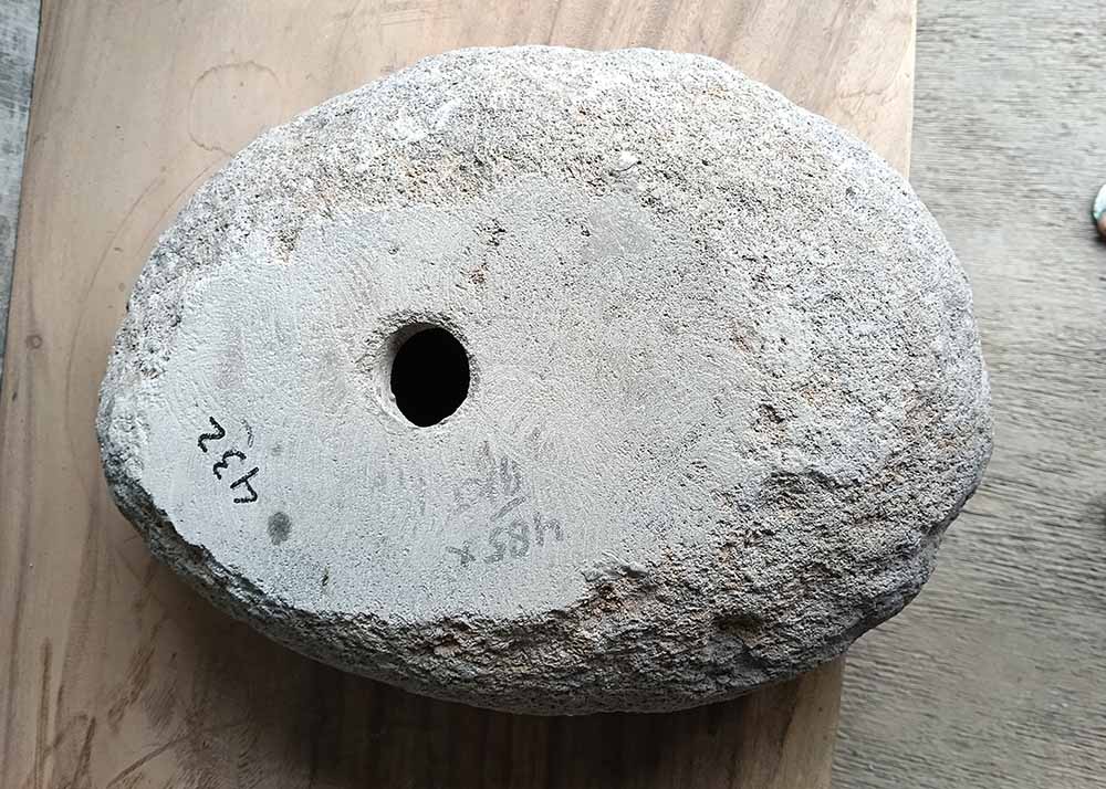 Bottom view of river stone sink showing central drain hole and raw base finish