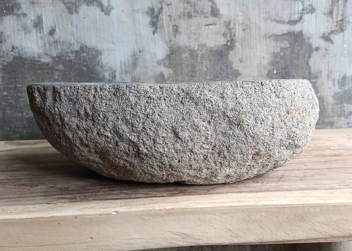Back side of a handcrafted stone basin showing rough stone surface