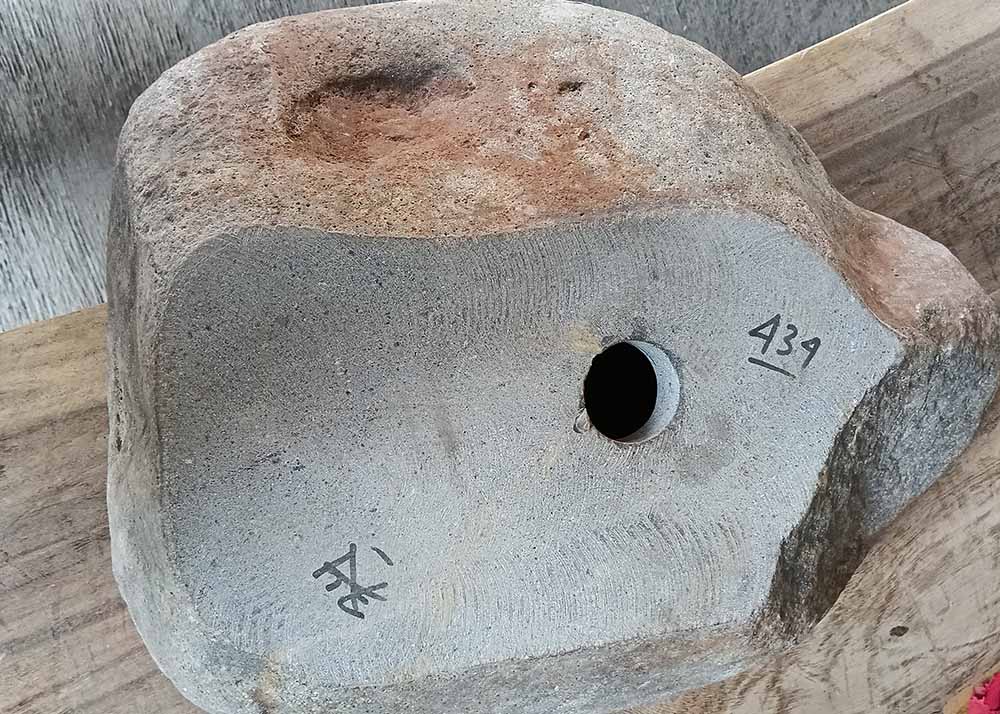 Underside of river stone sink with visible drain hole and unpolished natural stone base