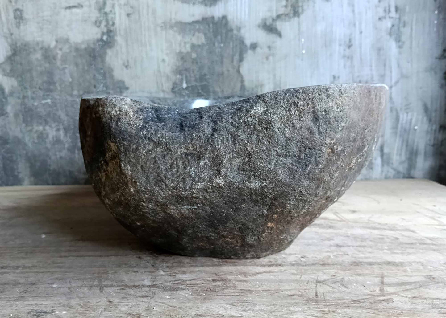 Right side view of rustic brown oval river stone sink with polished interior and rough exterior texture