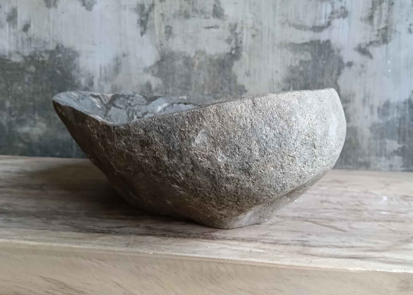 Left side of irregular river stone sink with layered natural striations and smooth polish inside