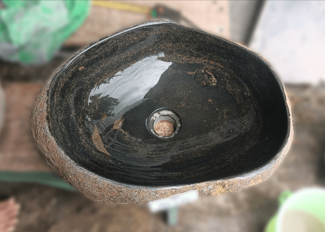 Top view of handcrafted river stone sink with dark grey and brown-streaked interior and rust-orange exterior