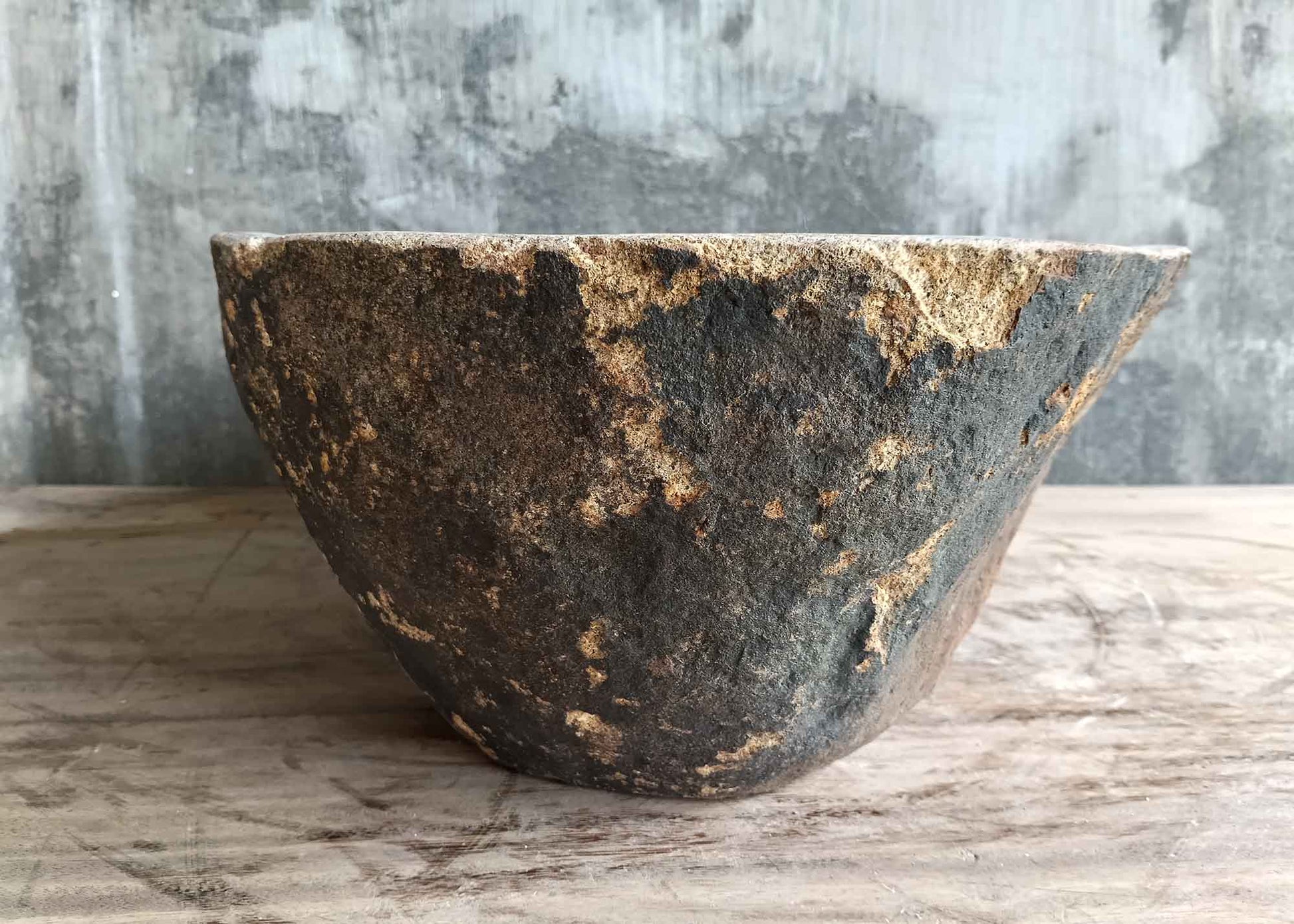 Left side view of handcrafted river stone sink with reddish raw texture and boat form
