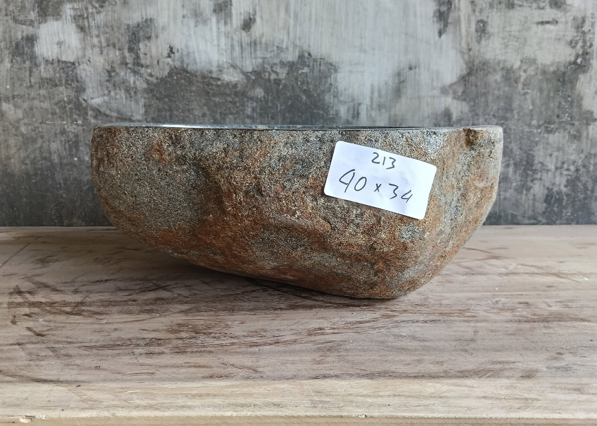 Side angle showing rough exterior of natural stone vessel sink in sculptural form
