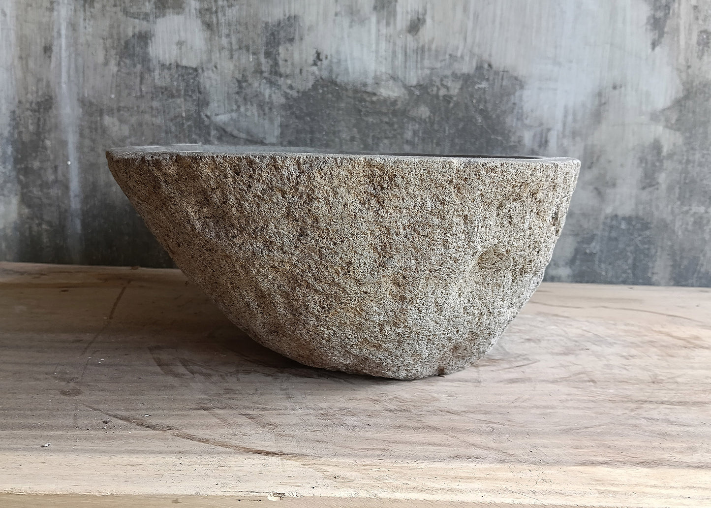 Right side view of handcrafted gray river sink with oval body and textured raw stone
