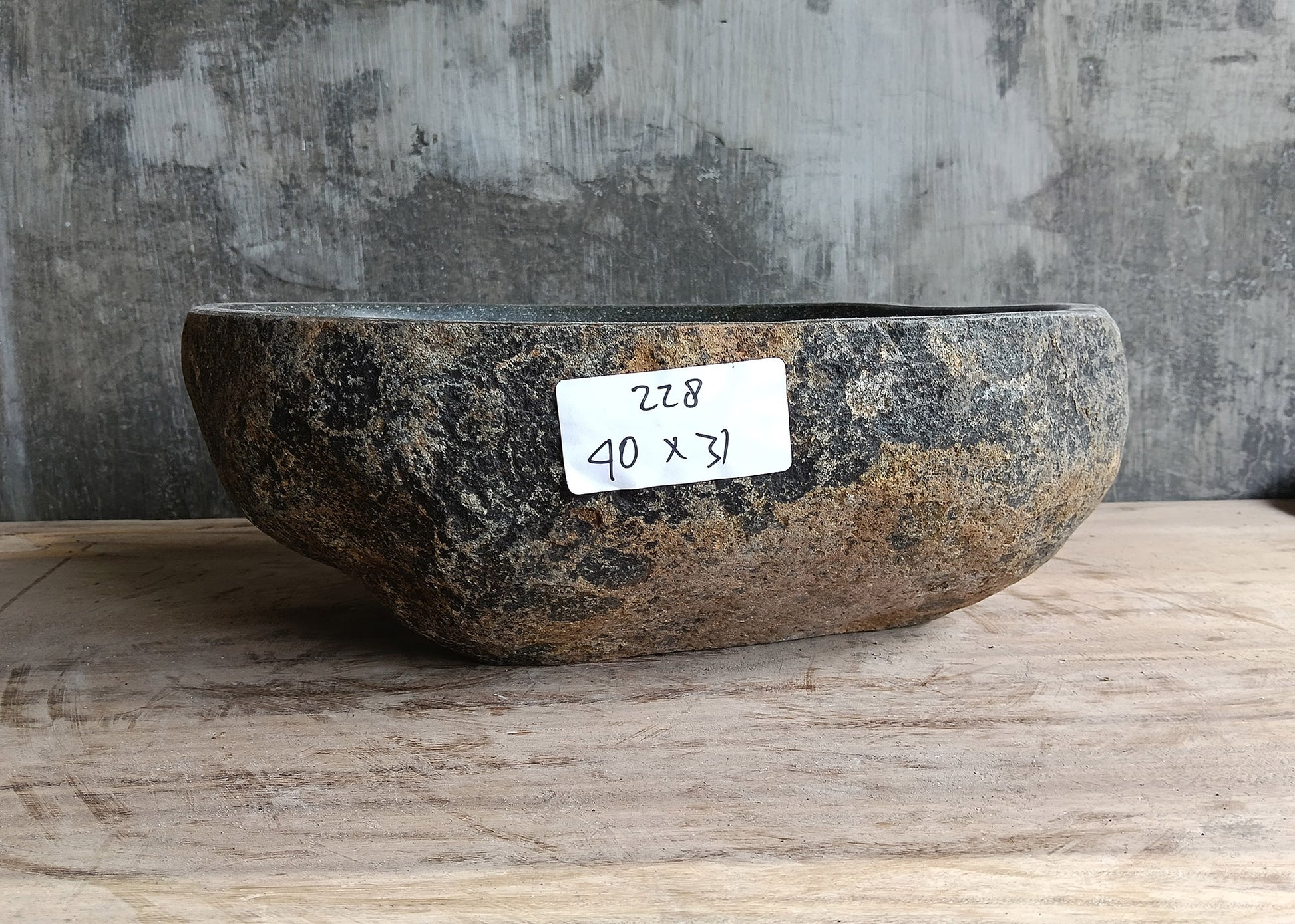 Front side of handcrafted dark gray stone sink showing curved oval profile and natural texture

