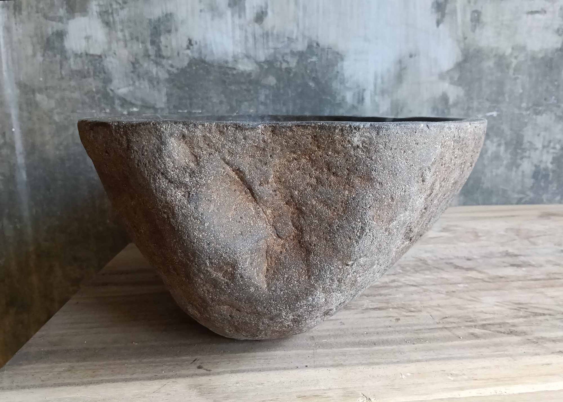 Right side of dark gray narrow stone sink with rugged exterior
