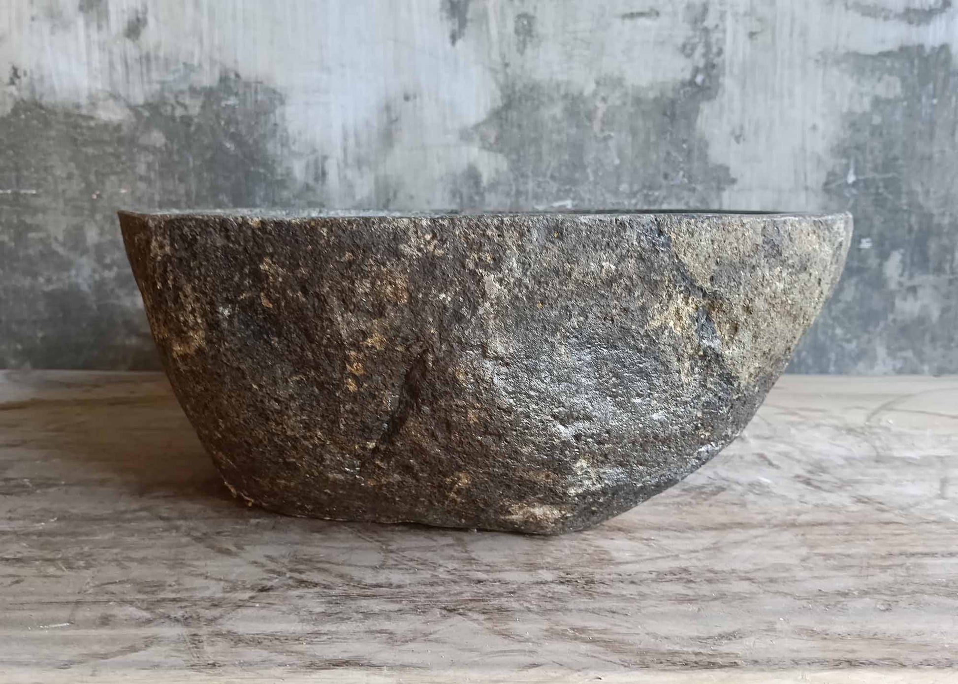Side profile of brown-gray river stone sink with curved silhouette
