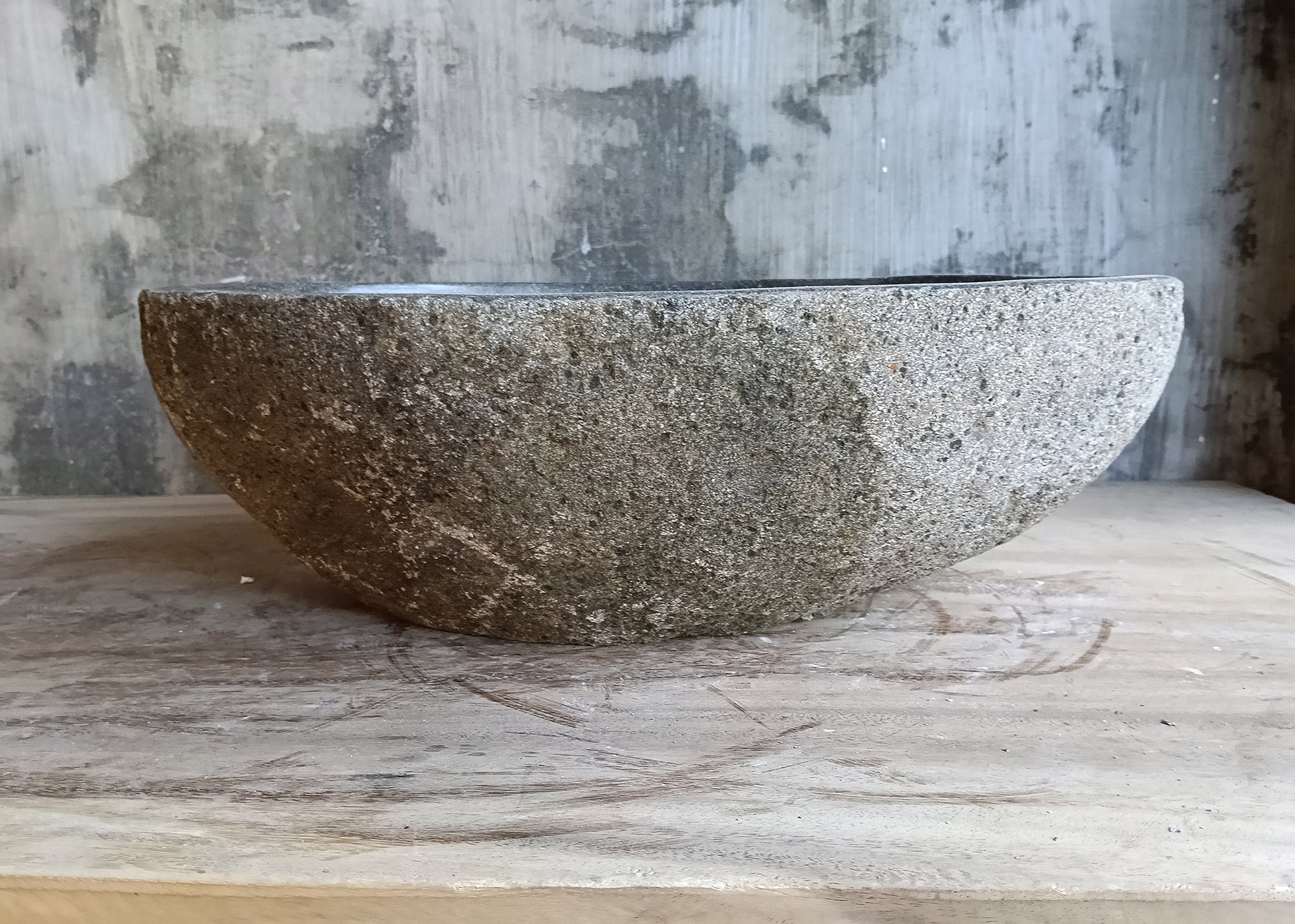Back side of oval river stone sink showing rough brown-gray stone finish
