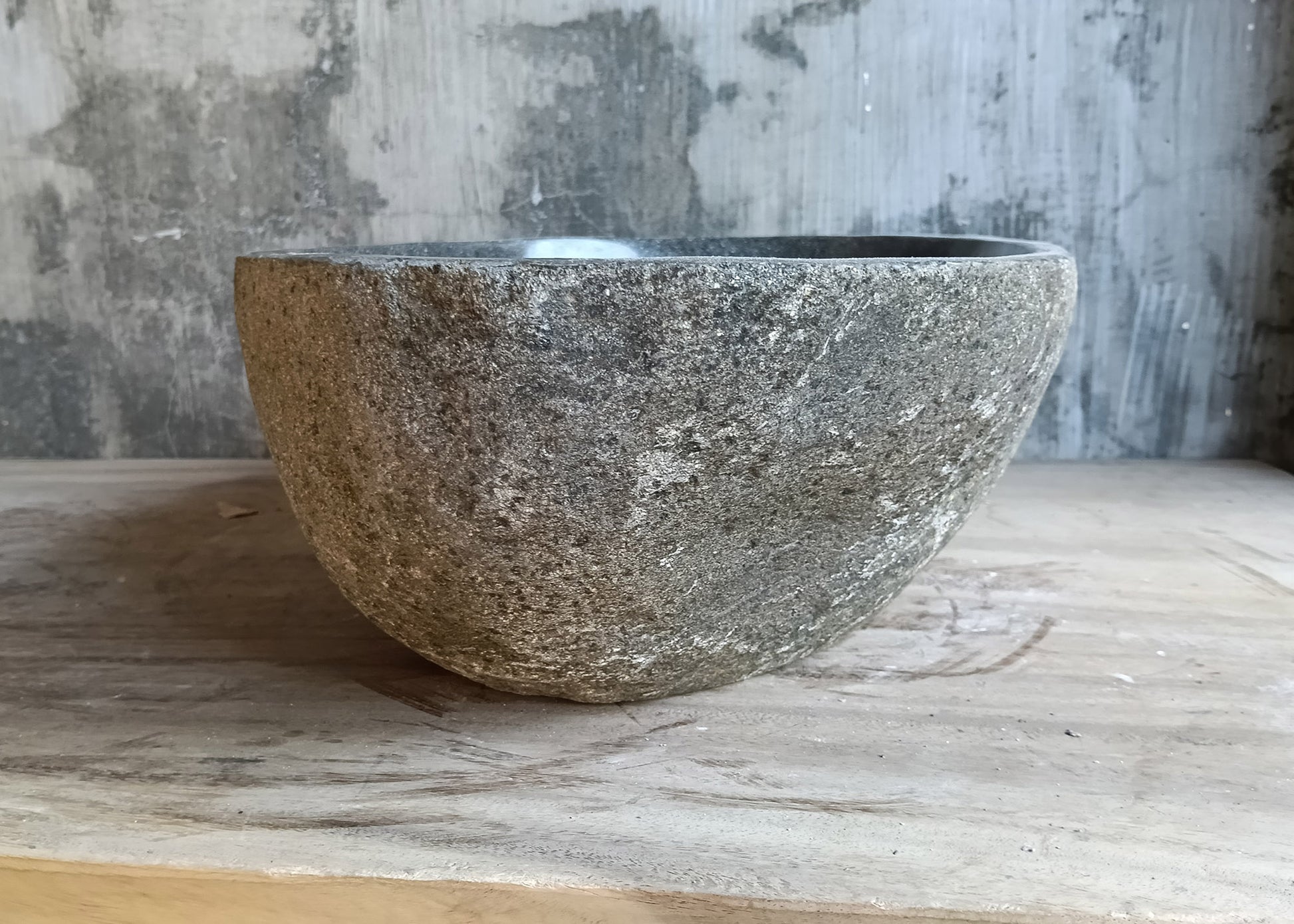 Right side of hand-carved stone basin with matte stone exterior and smooth interior curve
