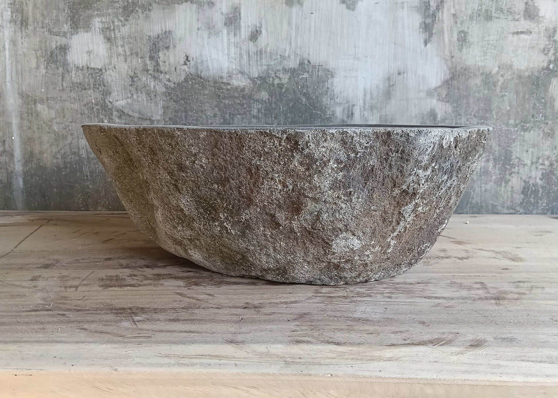 Left side of oval river rock sink with curved edges and polished gray bowl  
