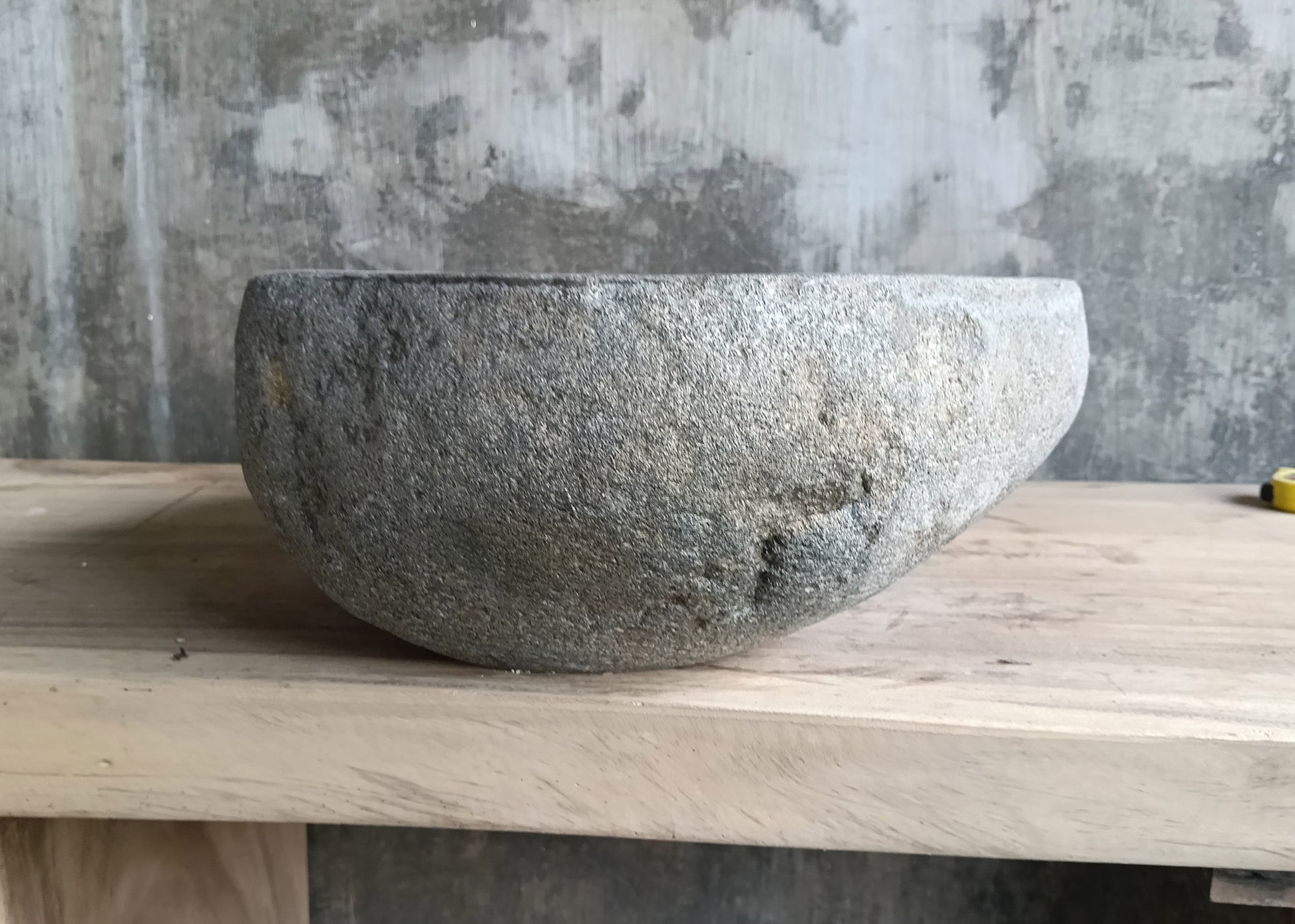 Right side of handcrafted gray river basin with raw stone finish and curved shape  
