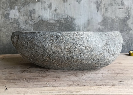 Front of handcrafted gray basin with natural rough exterior and uneven rim  
