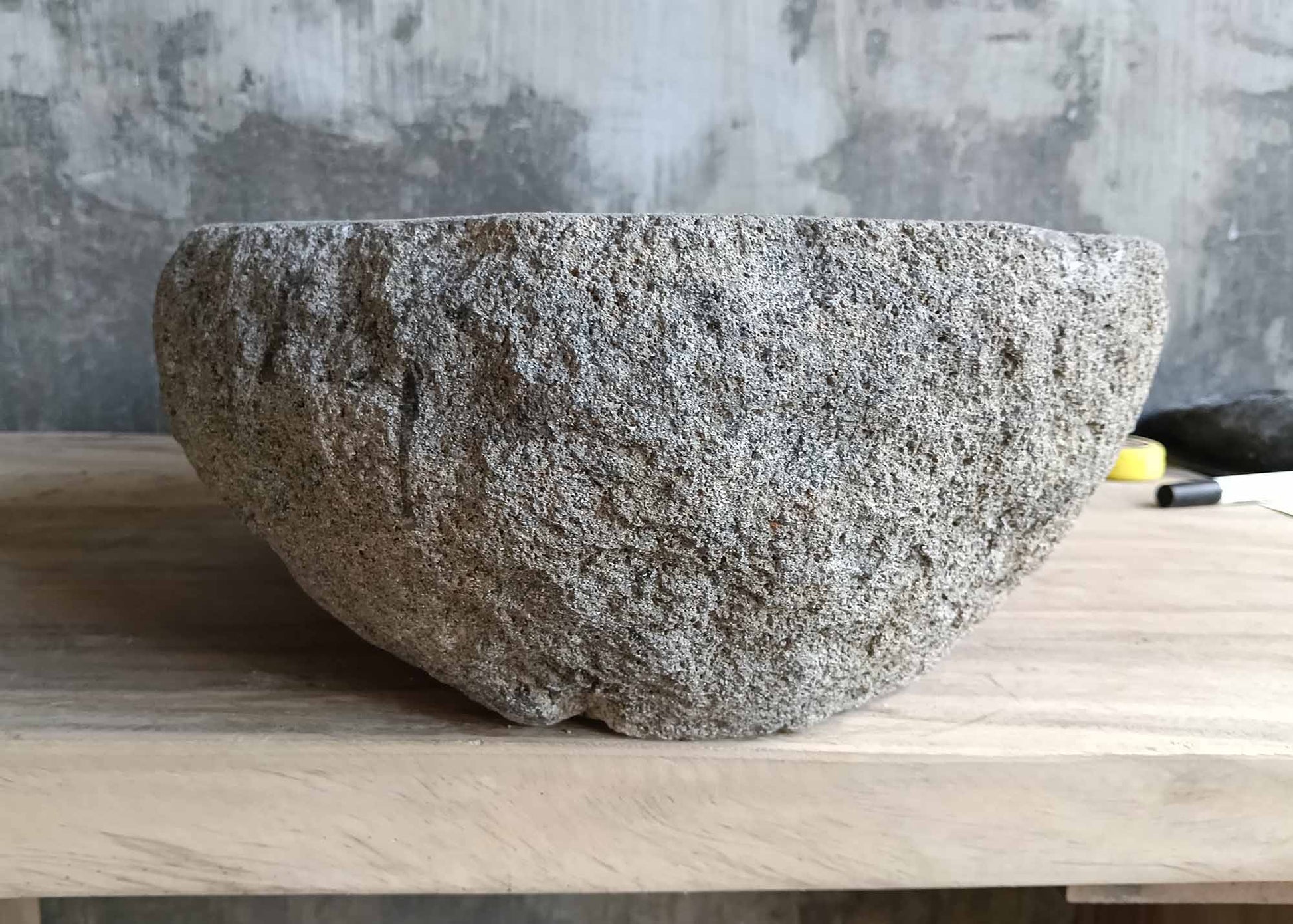 Left side of gray handcrafted sink with porous exterior and boat-like profile  
