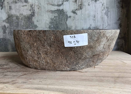 Front side of stone basin with raw textured surface and boat-shaped profile  
