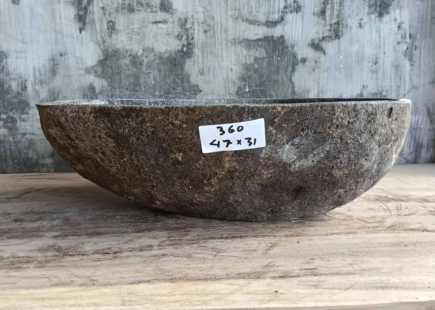 Front of natural river rock sink with boat-shaped contour and brown textured surface  
