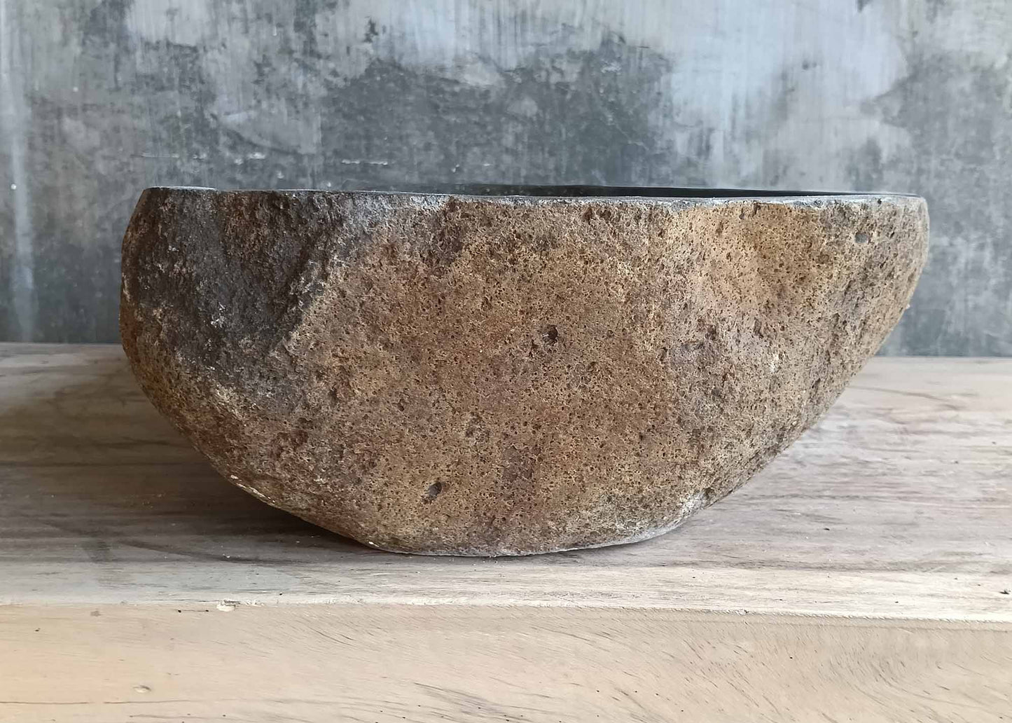 Left side of organic oval river stone sink with natural curve and raw exterior  
