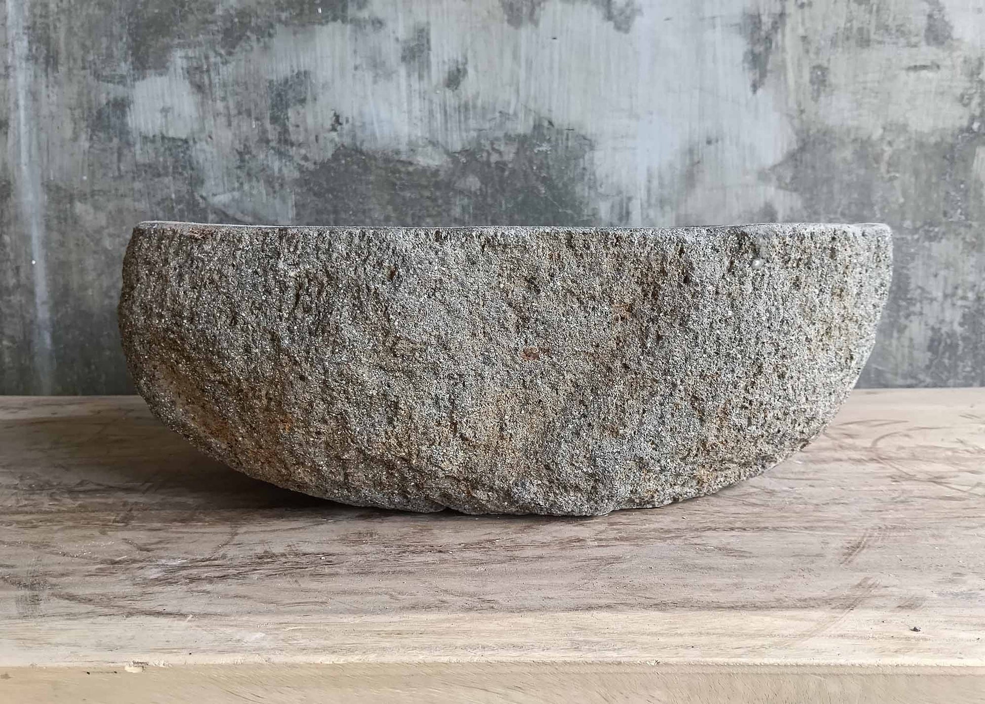 Back view of rustic sink with uneven contour and gray-brown natural stone body  
