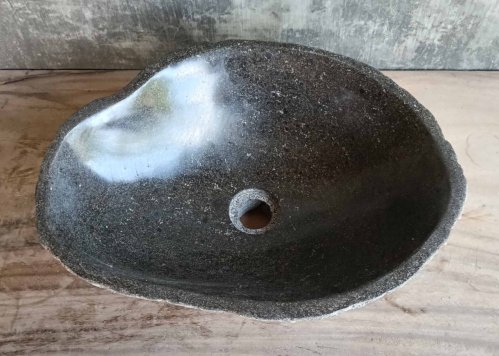 Side view of handcrafted grey river stone sink with rough natural texture
