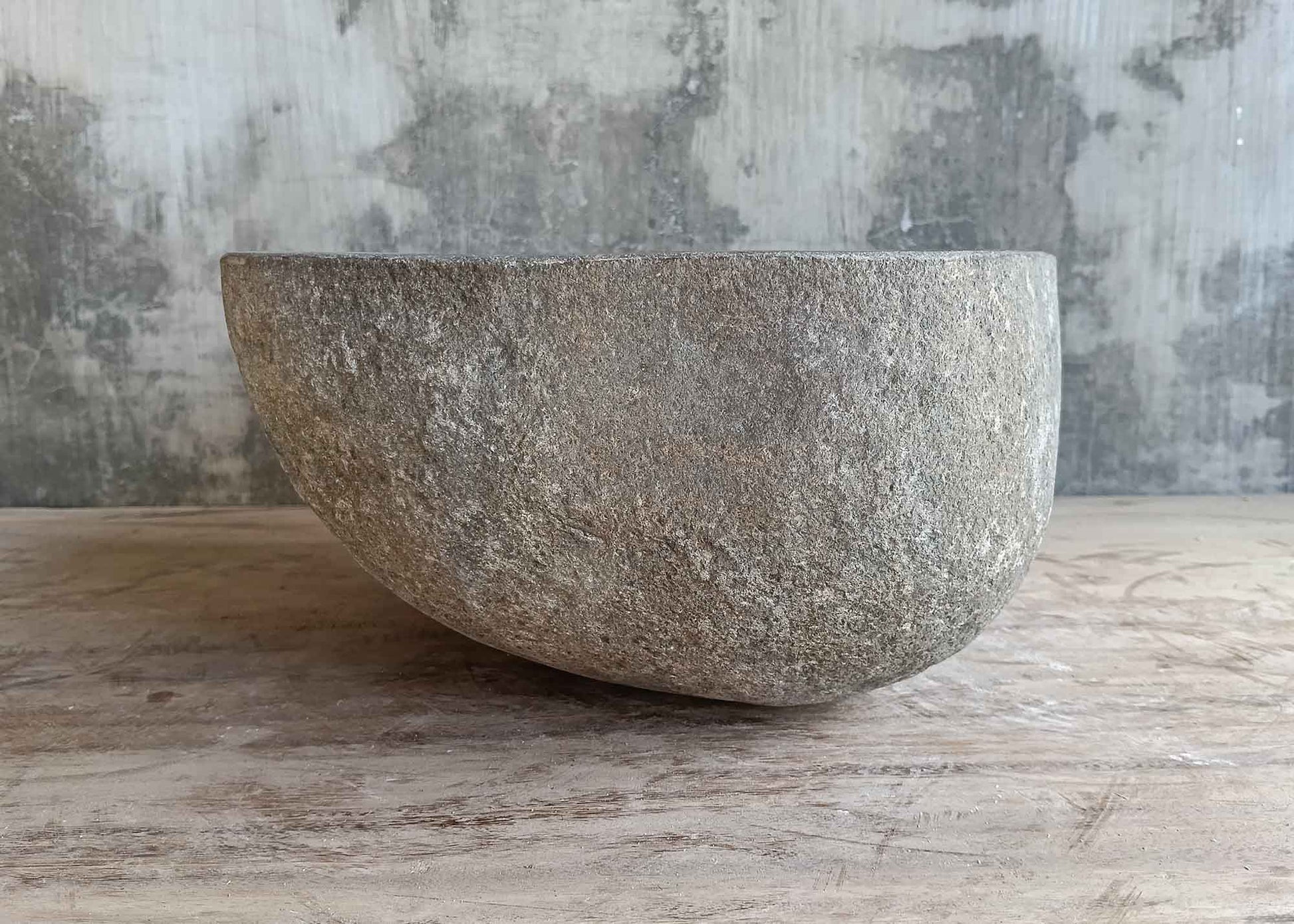 Left side of handcrafted round river stone sink in dark gray stone
