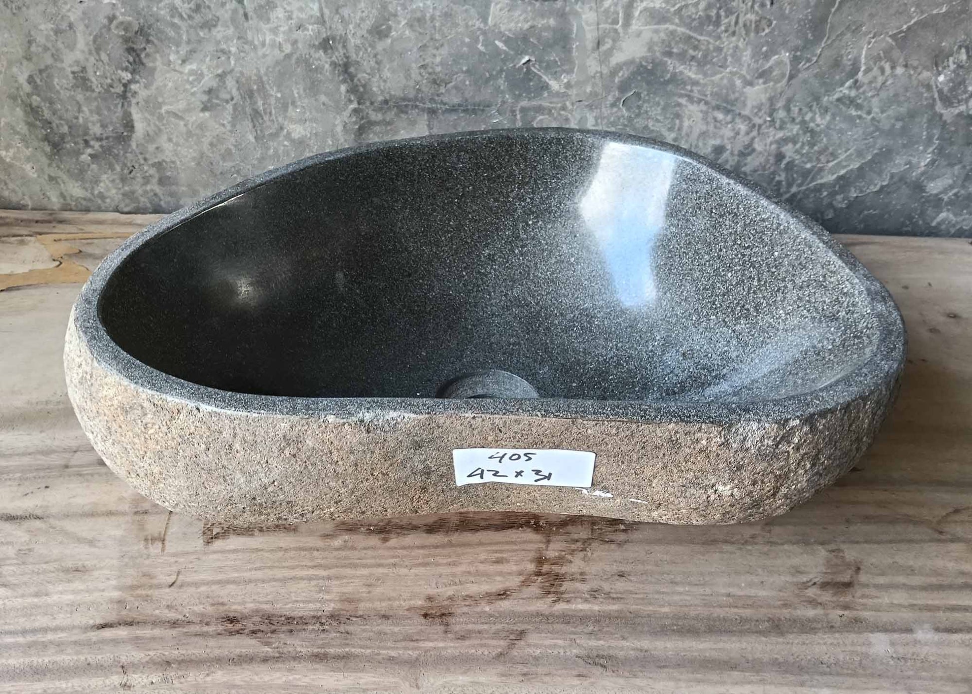 Interior view of river stone sink with deep gray polished surface and drain hole
