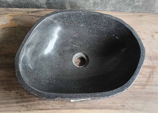 Top-down view of handcrafted river stone sink with deep polished basin and organic dark surface

