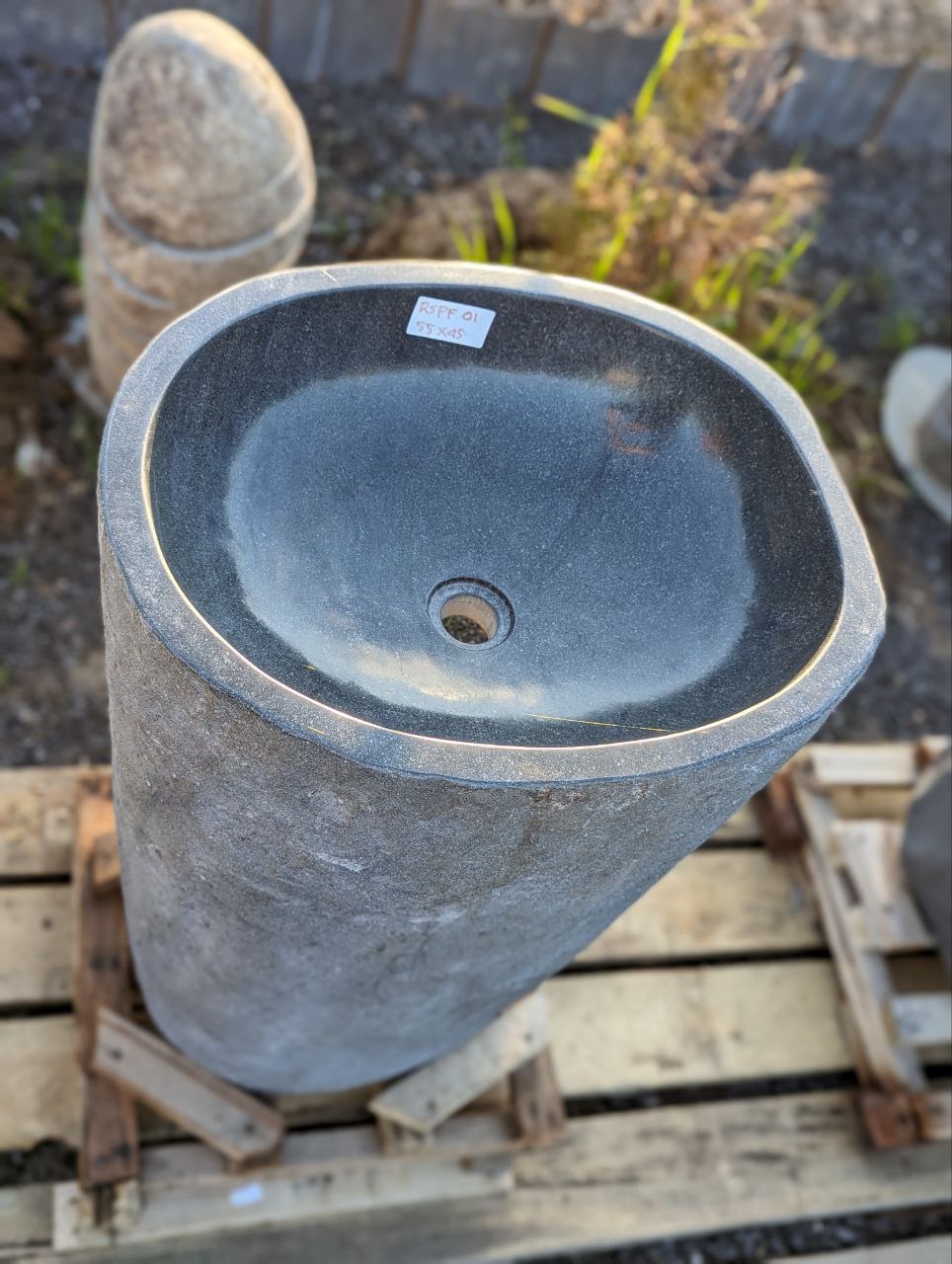 Side view showing textured gray exterior of river stone pedestal sink
