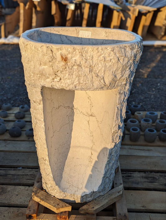 Side angle of natural marble pedestal sink with textured exterior
