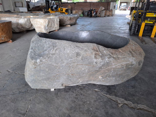 Side angle of natural river stone bathtub showing rugged exterior
