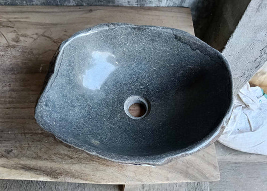 Top view of handcrafted oval brown river stone sink with polished dark interior and rugged natural exterior
