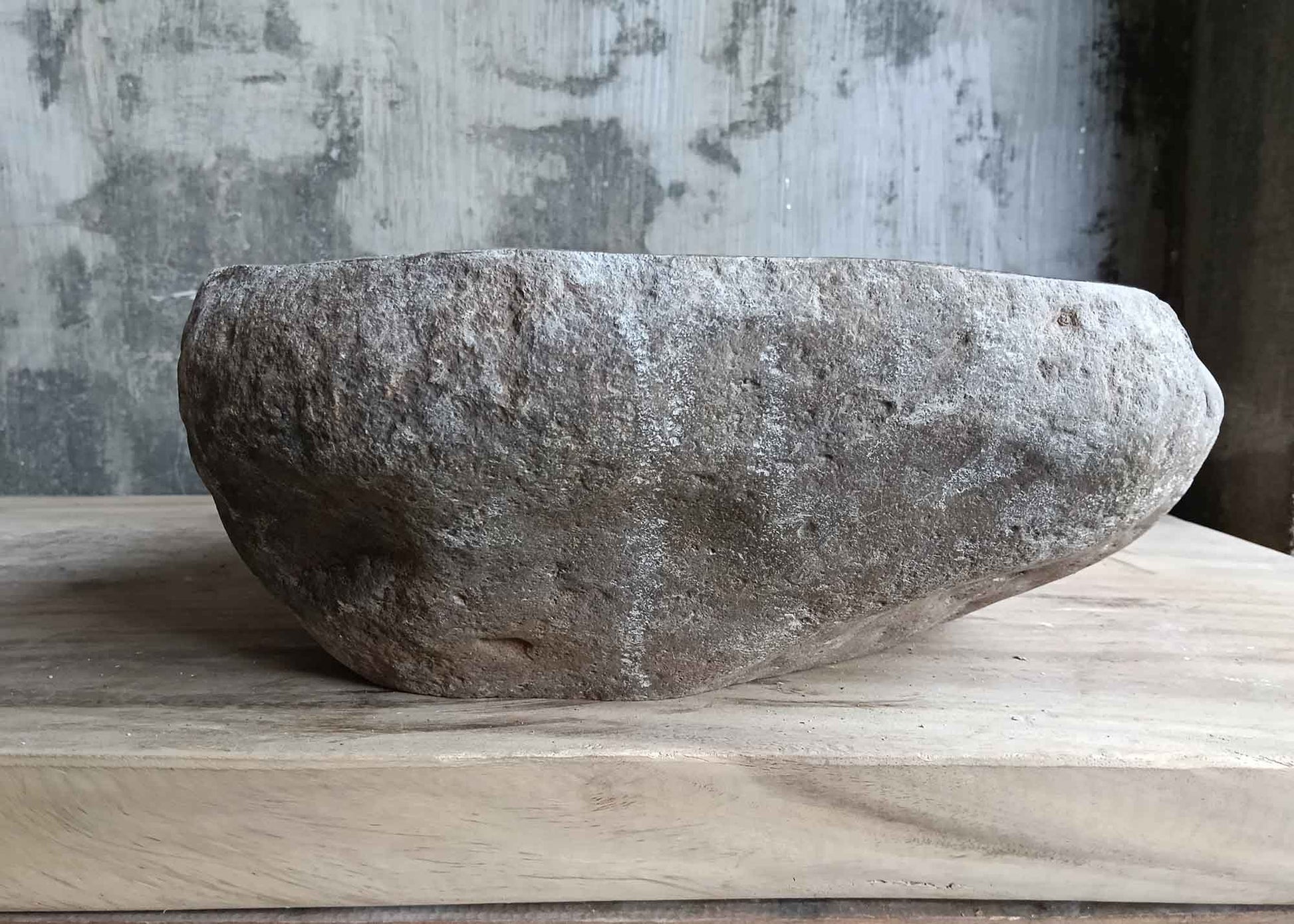 Left side view of gray handcrafted river stone sink with uneven organic contours
