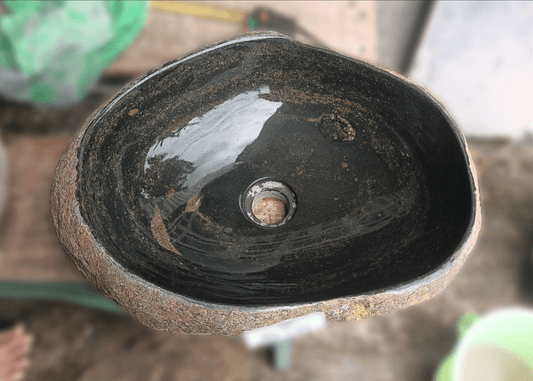 Top view of handcrafted river stone sink with dark grey and brown-streaked interior and rust-orange exterior

